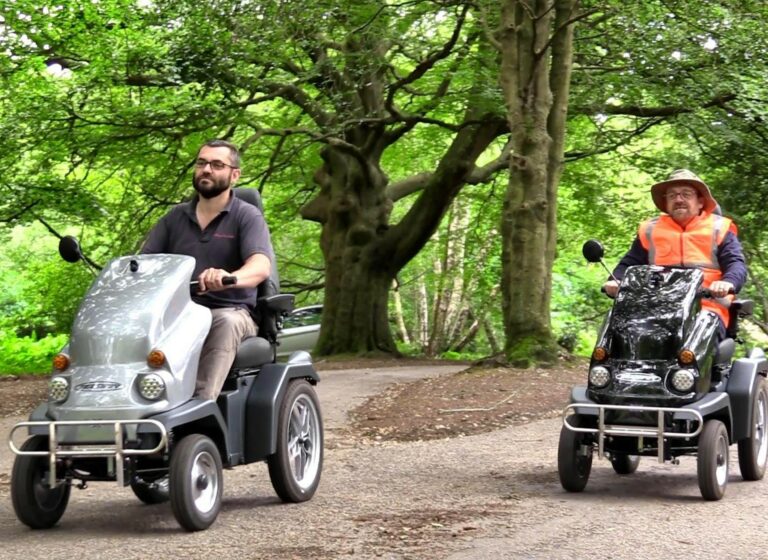Two trampers are driven through a woodland path, one man wears a hat and high viz jacket