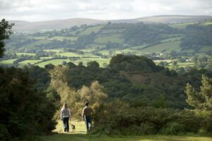 Walkers with dog on path at National Trust Castle Drogo. Rolling hills can be seen in the distance.