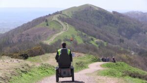 Man wearing hi-vis on tramper exploring the Malvern Hills. A path winds through the rolling hills with walkers sharing the path