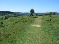 A path, covered in grass, with rolling hills in the distance at Crickley Hill Country Park.