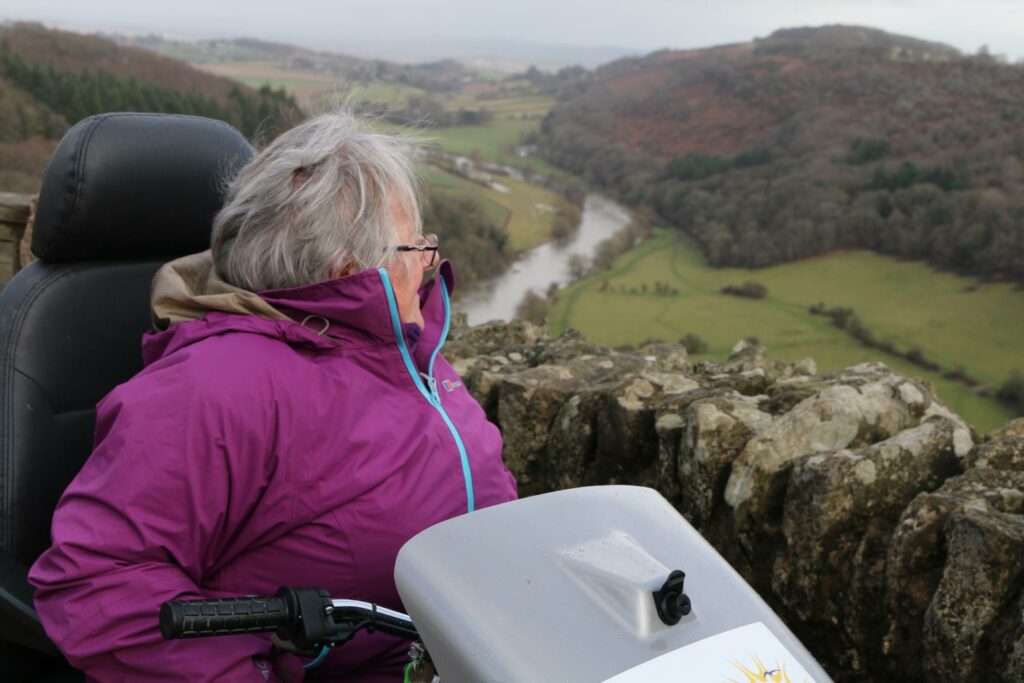 Lady on tramper looking out over the view of rolling hills and a river on a path in the Forest of Dean.
