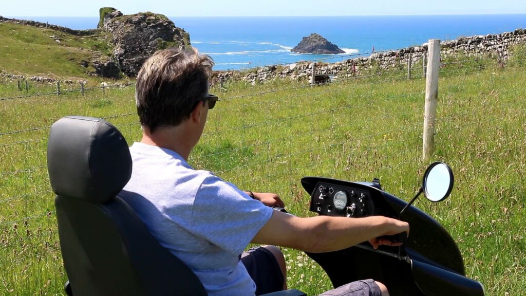Man in tramper enjoying coast view from the path at National Trust Pentireglaze on a warm sunny day.