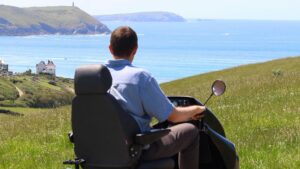 Man in tramper looking out to sea at National Trust Pentireglaze. The grass is green and sea and sky clear and blue