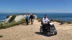 Man in tramper at National Trust Studland. Behind him is the coast leading to the sea. A sailboat can be seen in the sea and in the far distance another coast.