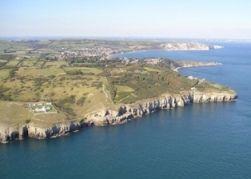 A coastal view from the air showing cliff sides, open sea and green fields