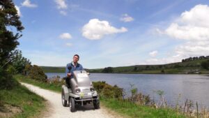 Man on tramper on path at Siblyback Lake Country park. The lake can be seen behind him, surrounded by rolling hills.