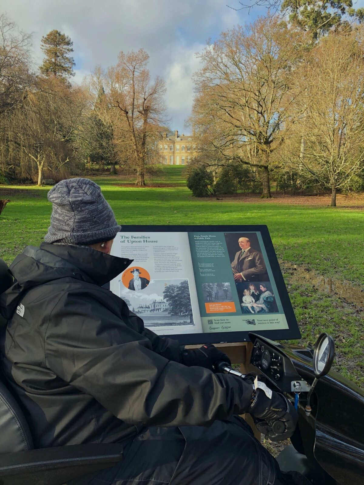 Mobility scooter user looking at information board with mansion house in the background at Upton Country Park