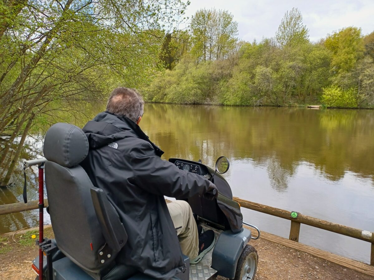 Visitor on all terrain mobility scooter looks out over a small lake