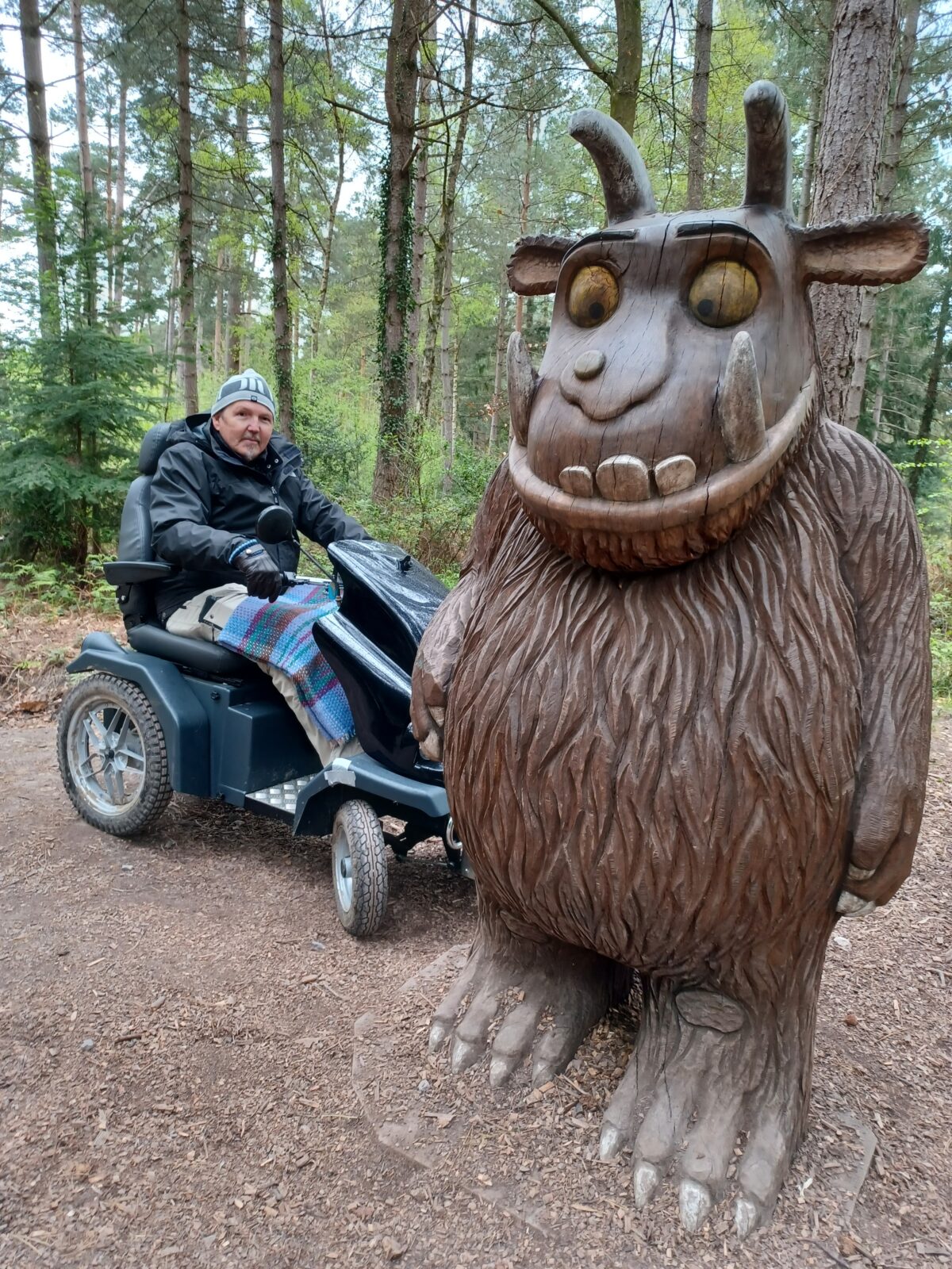 Visitor sits on all terrain mobility scooter next to Gruffalo sculpture