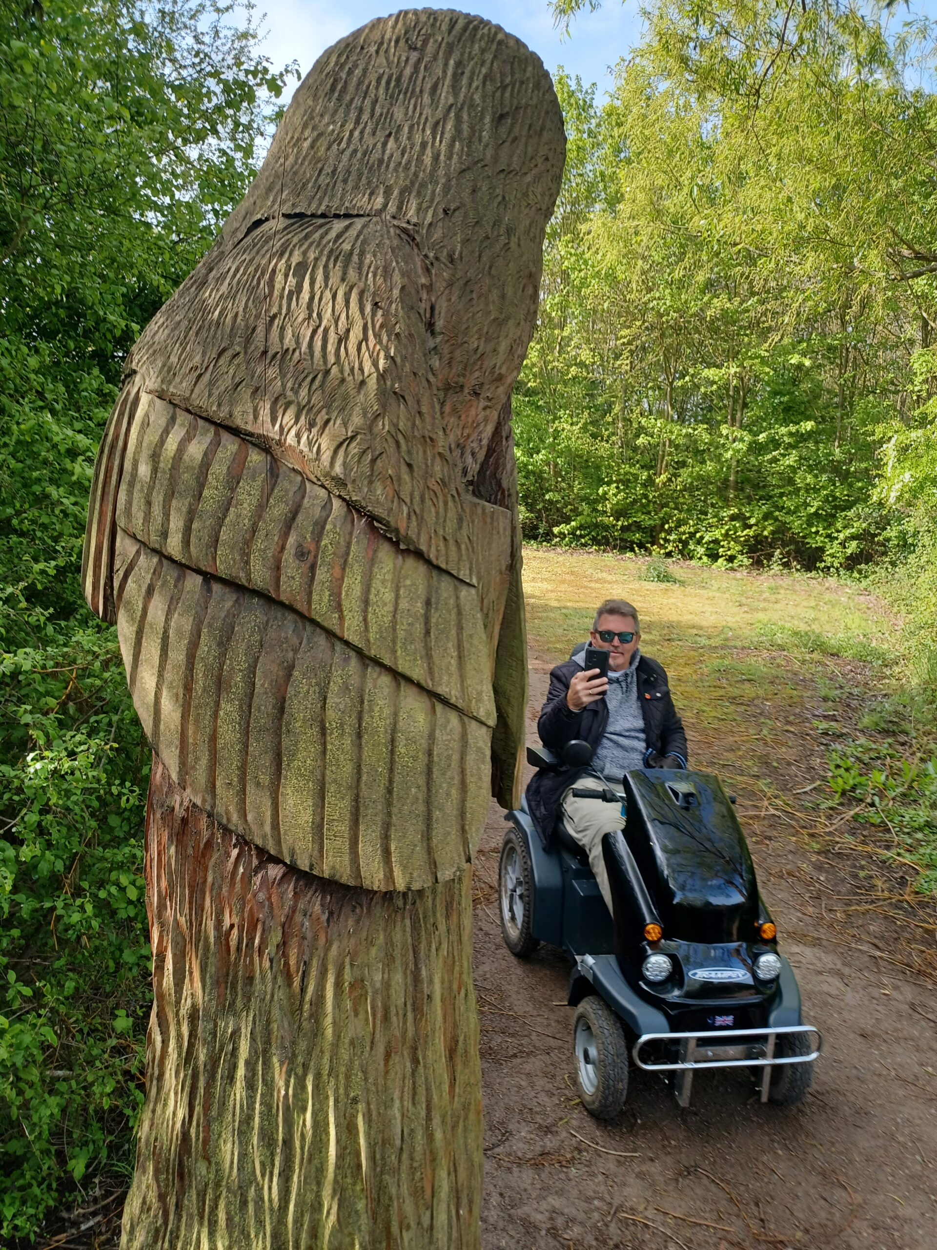 Man sat on a Tramper all terrain mobility scooter takes a photo of a wooden sculpture