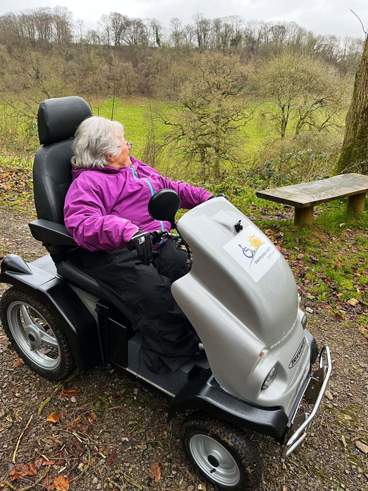 Visitor sits on all terrain mobility scooter looking at a view across a wooded valley