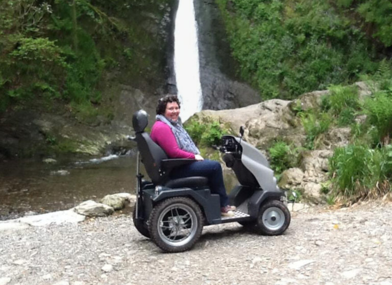 Woman smiling on a Tramper, with a waterfall behind her.