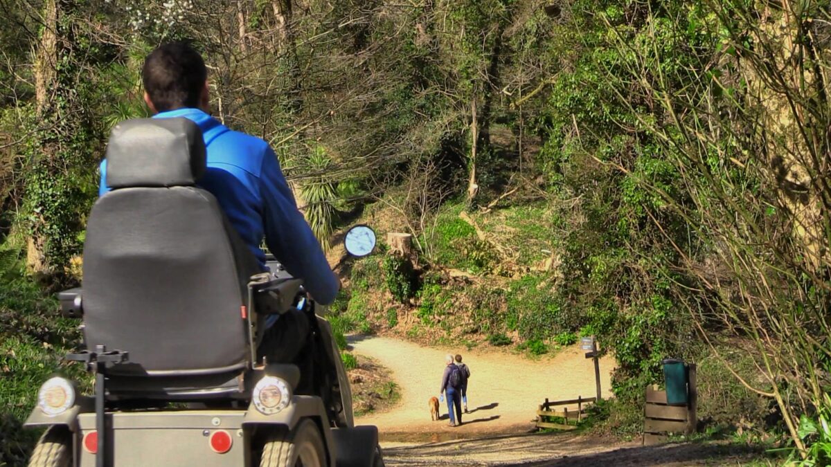 All terrain mobility scooter drives downhill in a woodland at the Lost Gardens of Heligan
