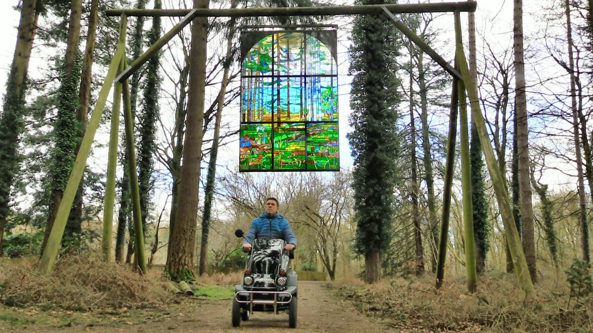 All terrain mobility scooter passes beneath a stained glass window hanging from trees