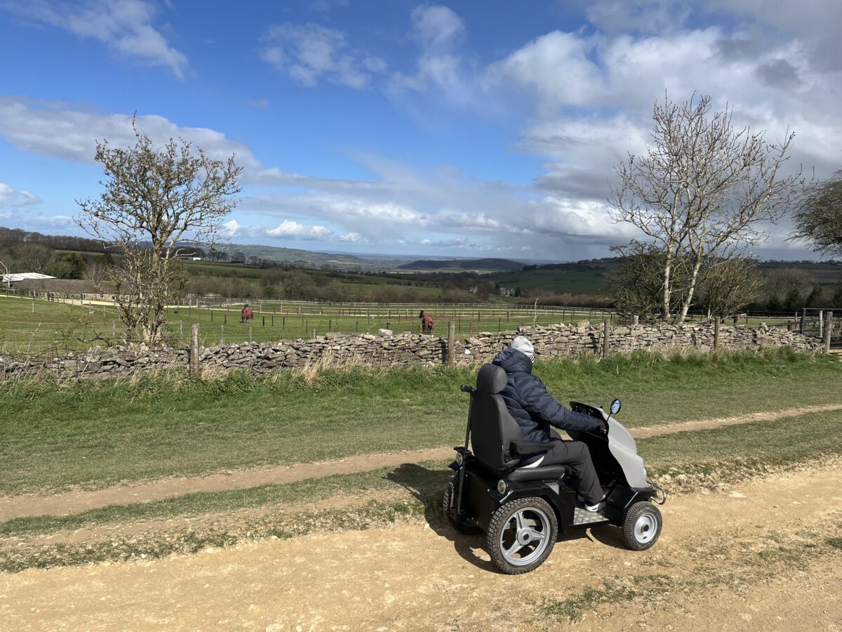 Man on all terrain mobility scooter looks at view beyond a dry stone wall.