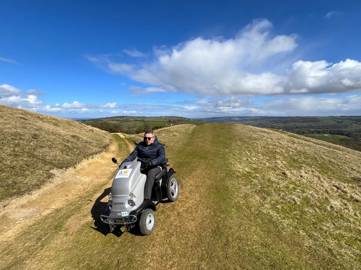 Man on all terrain mobility scooter leaves viewpoint in the background.
