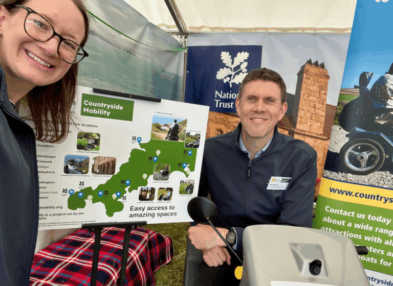 Emma and Neil smile next to a Cornwall map with Countryside Mobility locations highlighted.