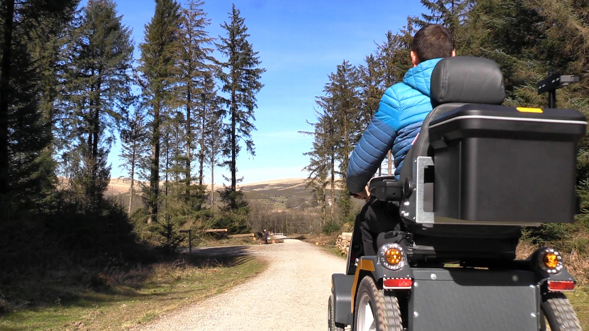 All terrain mobility scooter goes along a forest track with moorland in the background