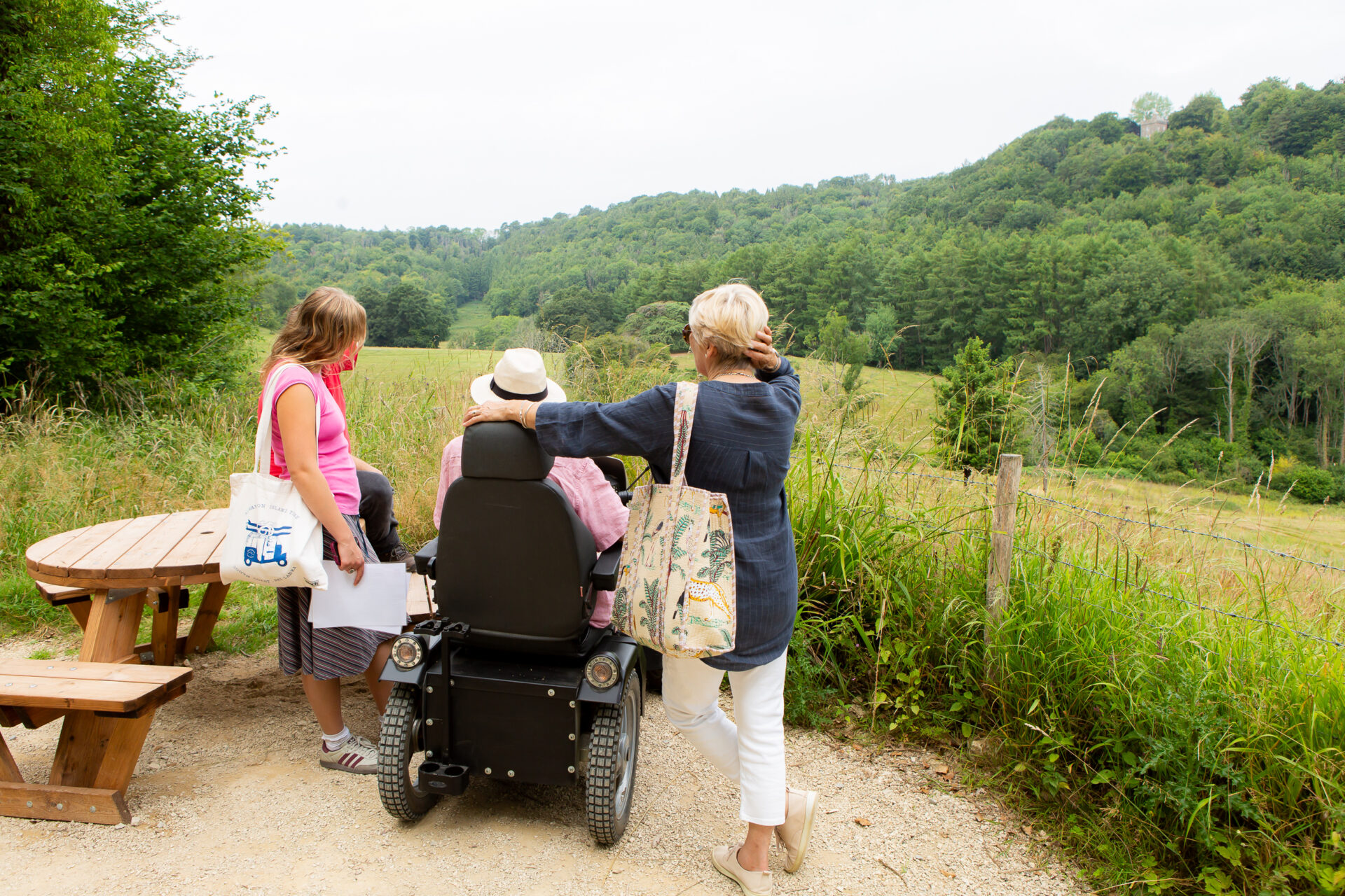 Loxie, Val, and Mike are together looking out at the landscape. There are many trees and fields. Mike is on a Tramper