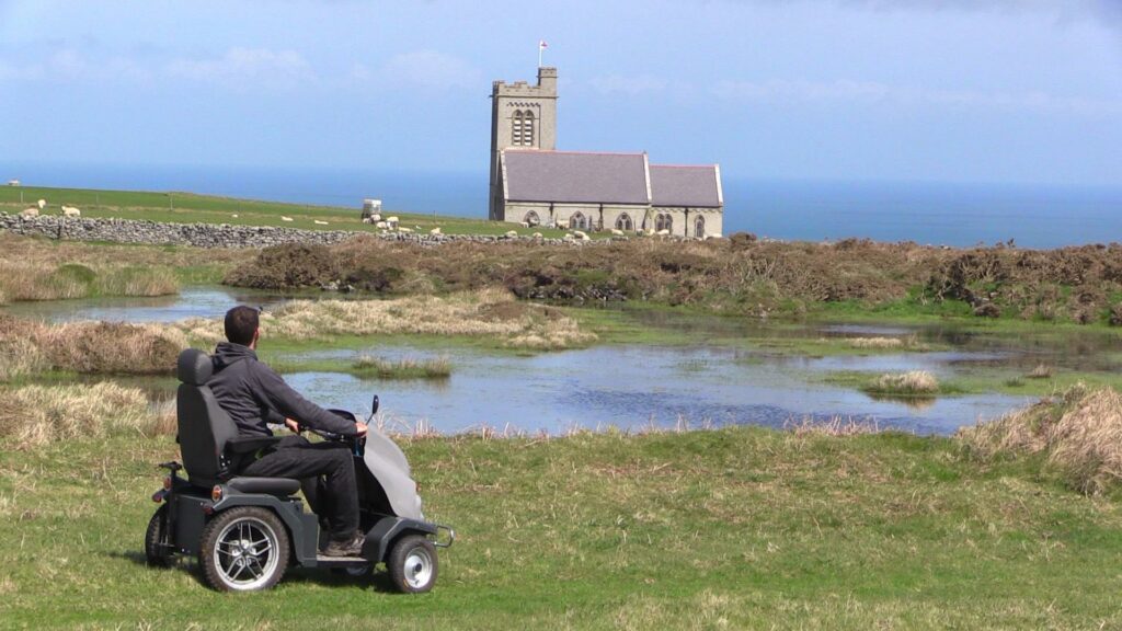 Man in tramper exploring Lundy Island. You can see a church and some sheep. 