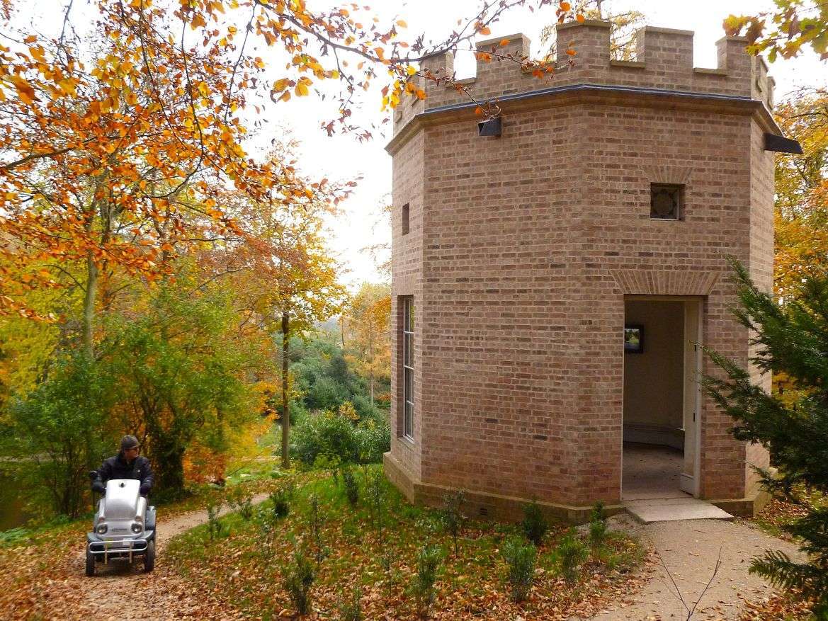 Man on Tramper passing by historic Hestercombe building, surrounded by orange autumn trees.